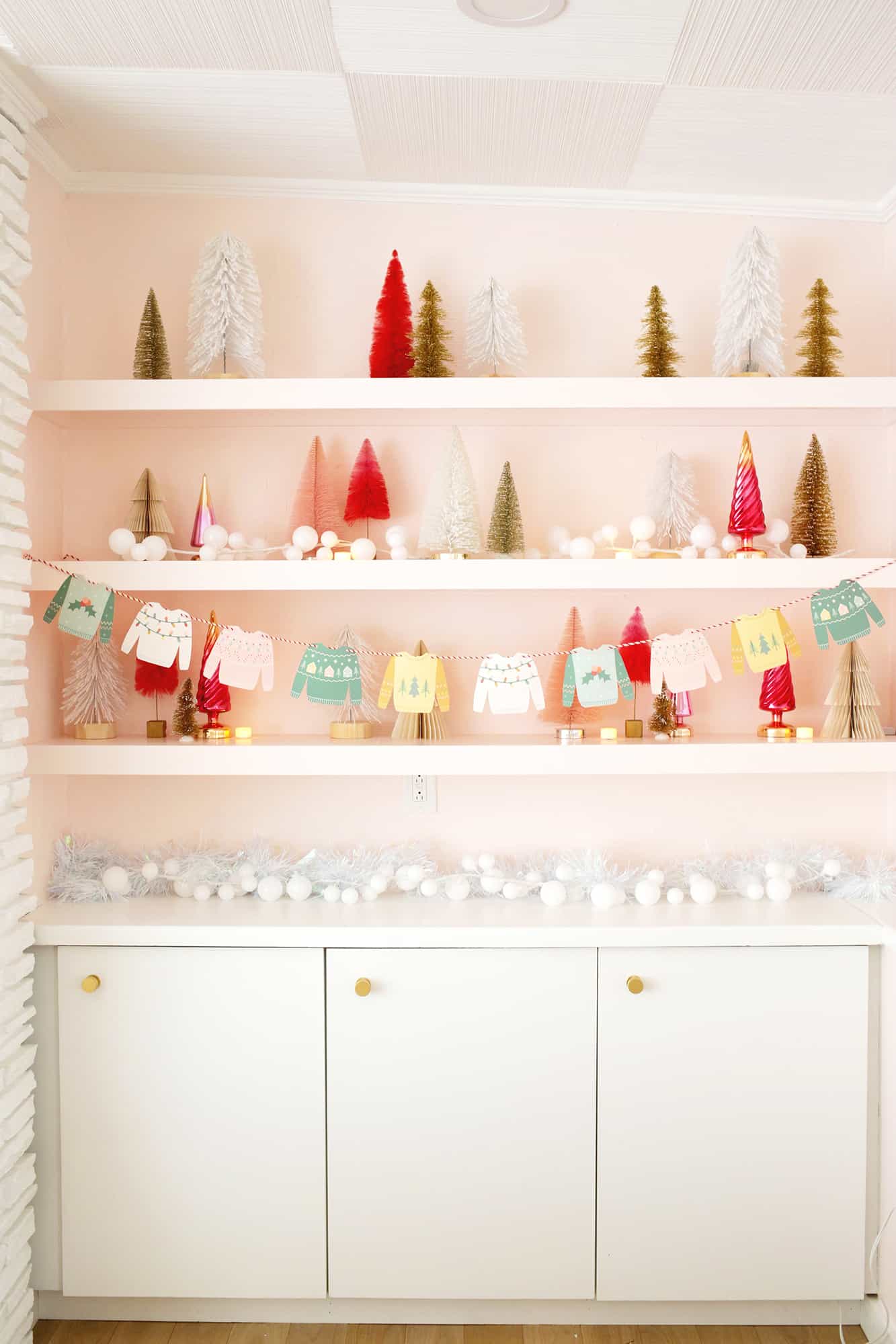 Paper Christmas sweaters strung on a garland with Christmas tree shelf decor
